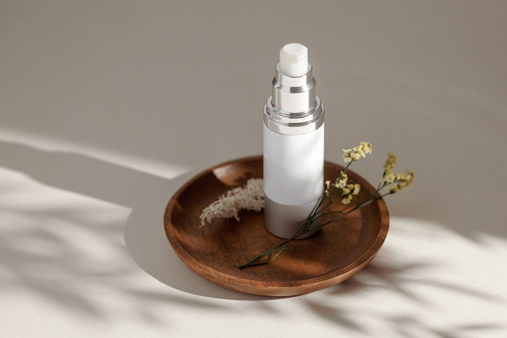 Illustrative fragrance bottle on a wooden tray beside flowers in soft natural light