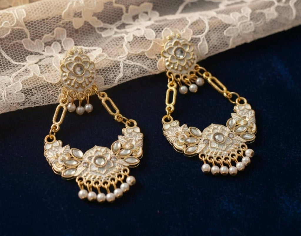 Gold and pearl earrings on a dark surface with lace fabric in the background