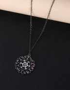 A silver filigree pendant necklace with a floral center, displayed on a black surface with a cream-colored background at the top.