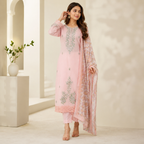 A woman models a light pink traditional outfit with silver-gray floral embroidery, matching trousers, and a sheer patterned dupatta in a bright, modern architectural setting.