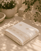 Ivory cotton shawl with gold embroidered border and small motif corners, folded.