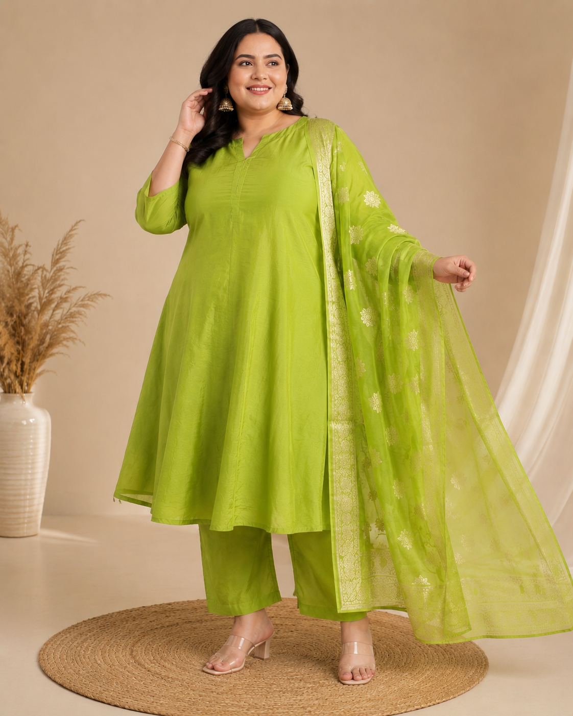 A woman models a bright lime green three-piece ethnic suit consisting of a kurta, pants, and a matching sheer dupatta with gold border and floral prints, set against a warm beige background.