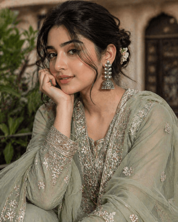 Woman in traditional attire with floral earrings, sitting outdoors.