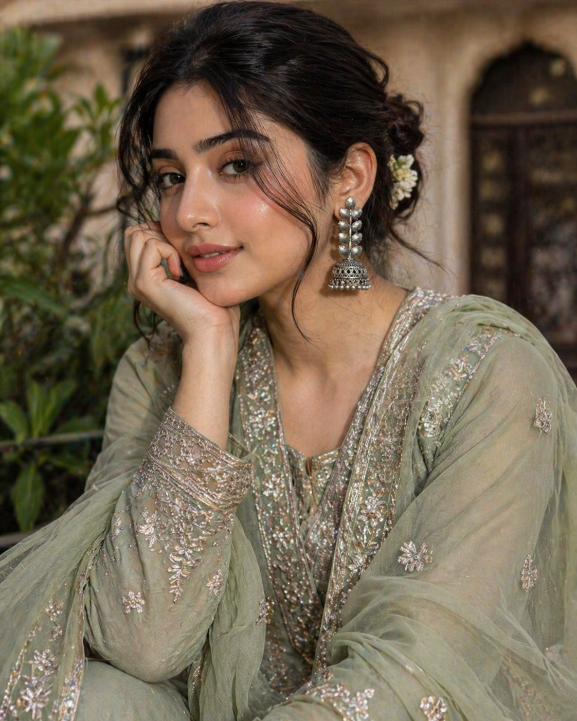 Woman in traditional attire with floral earrings, sitting outdoors.